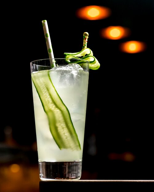 A glass of cocktail with cucumber with ice and paper straw