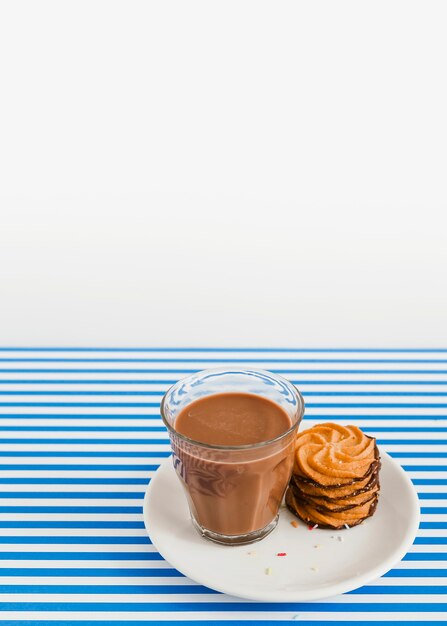 Glass of coffee and stack of cookies on plate over white and stripes background