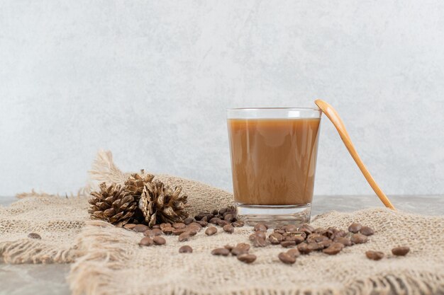 コーヒー豆と黄麻布のスプーンとコーヒーのグラス。