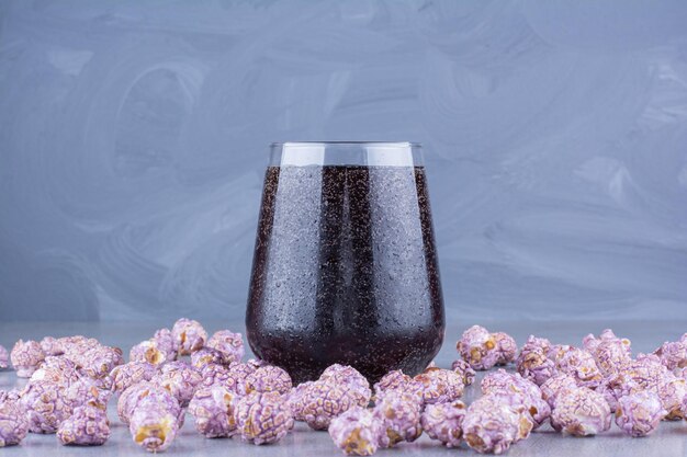 Glass of cola surrounded by scattered popcorn candy on marble surface