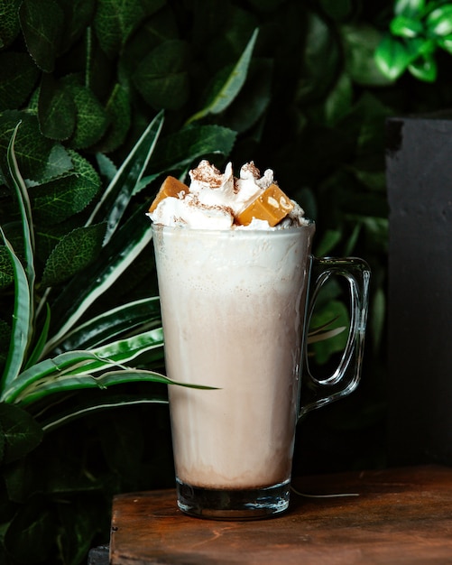 A glass of cold coffee drink garnished with whipped cream and caramel with nuts