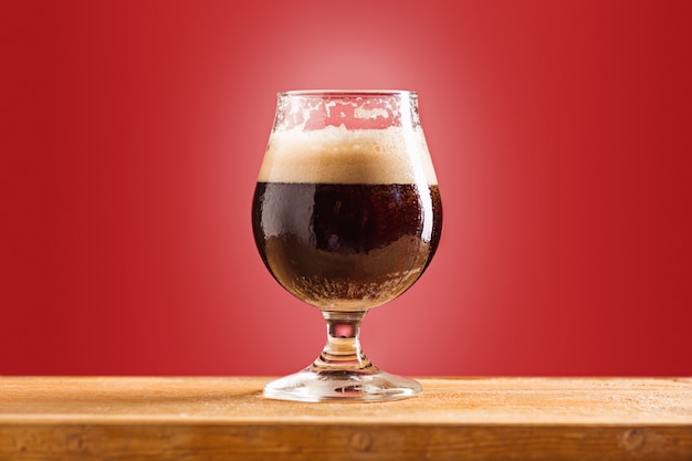 Glass of cold frothy dark beer on an old wooden table