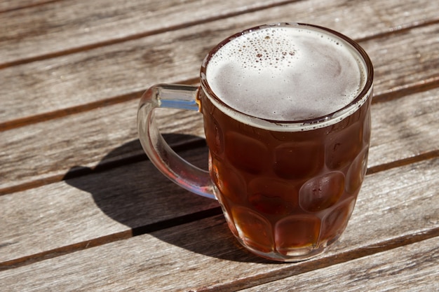 Glass cup of cold beer on a wooden surface on a hot sunny day