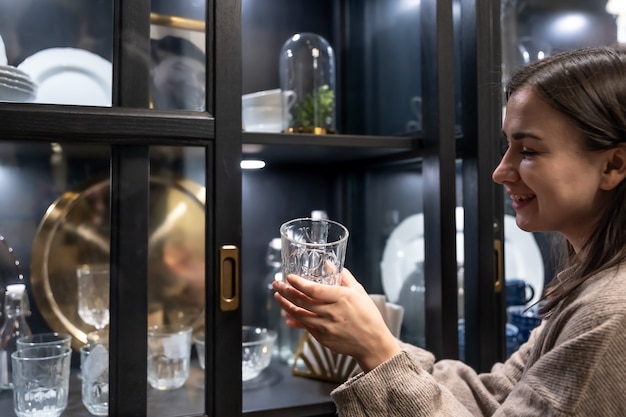 Glass cup in female hands on the background of a sideboard with beautiful vintage dishes.