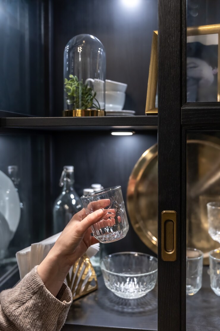 मुफ़्त फोटो glass cup in female hands on the background of a sideboard with beautiful vintage dishes.