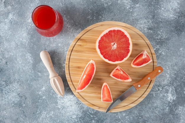 Glass cup of fresh grapefruit juice with slices of fruits and wooden reamer . 