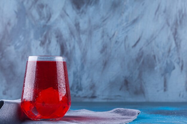 A glass cup of fruit juice with ice cubes placed on a sackcloth surface