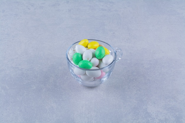 회색 표면에 다채로운 콩 사탕으로 가득 찬 유리 컵. 고품질 사진