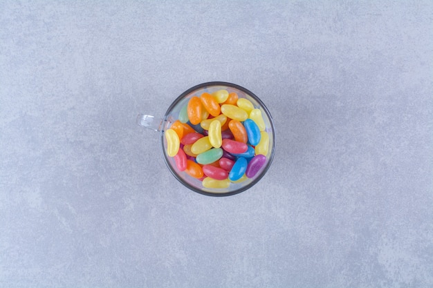 A glass cup full of colorful bean candies . 