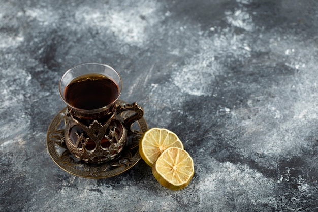 A glass cup of hot tea with slices of lemon . 