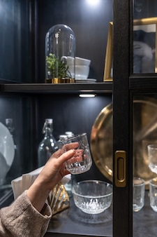 美しいヴィンテージ料理とサイドボードの背景に女性の手でガラスのカップ。