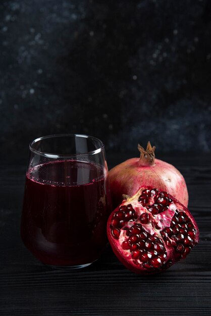 A glass cup of juice with pomegranate on dark. 