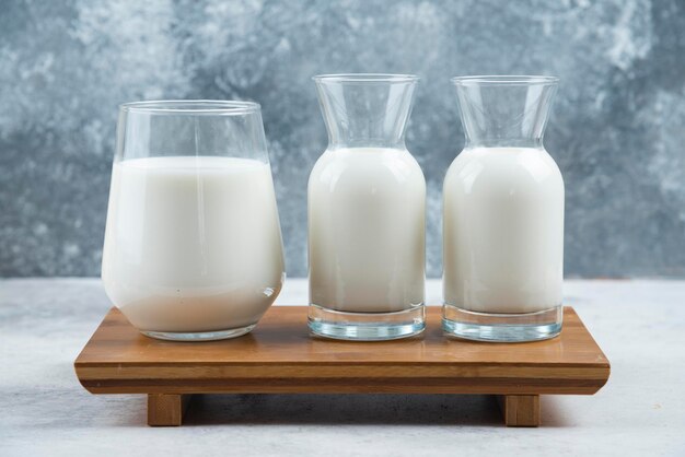 A glass cup of milk and two glasses jar of milk on a wooden small desk.