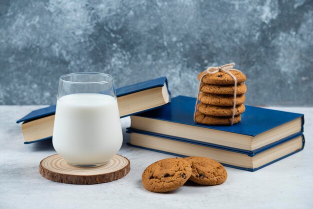 A glass cup of milk with chocolate cookies on a wooden board.