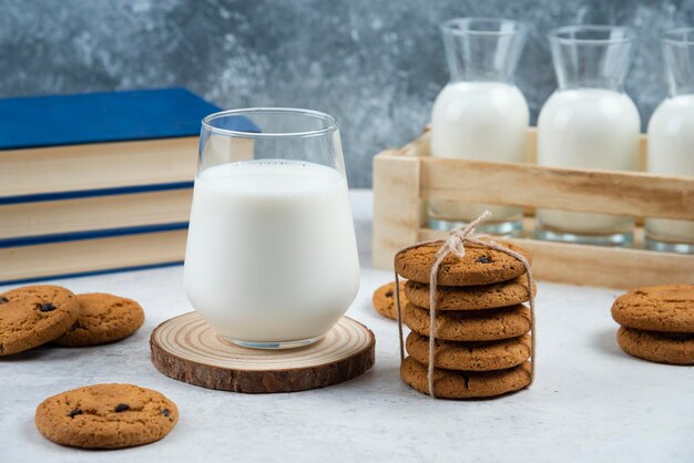 A glass cup of milk with chocolate cookies on a wooden board.