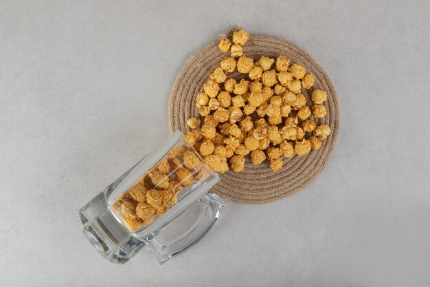 Glass cup of popcorn candy spilling over a trivet on marble surface. 