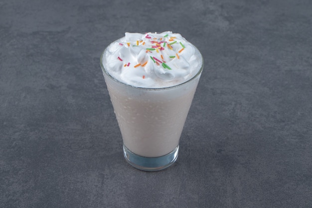 A glass cup of sweet milkshake with whipped cream . 