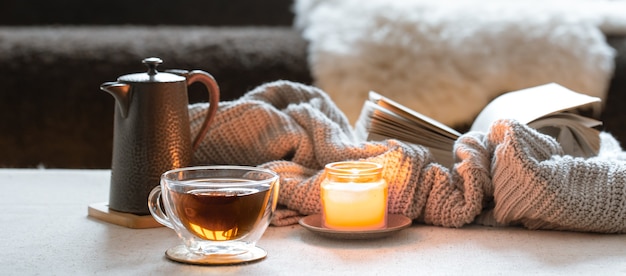 차, 주전자, 촛불 및 니트 요소와 책의 유리 컵. 가정의 편안함과 따뜻함의 개념.
