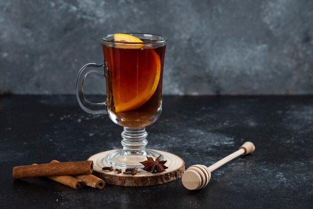 A glass cup of tea and with cinnamon sticks and wooden dipper.