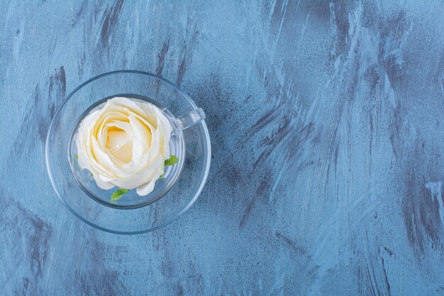 青い上に置かれた白いバラのガラスのカップ。