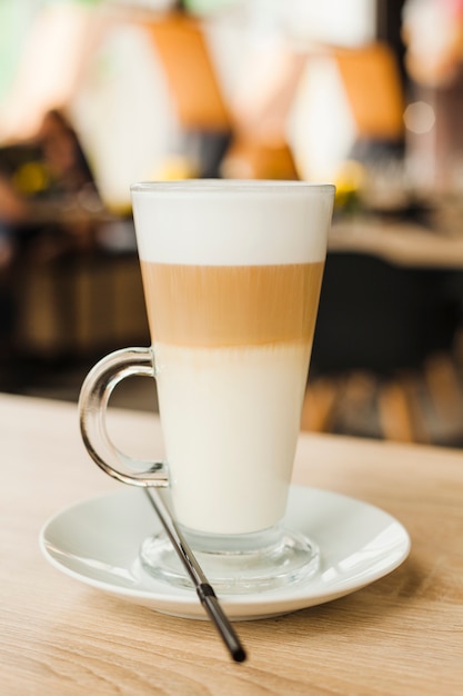 Glass cup with hot latte on wooden table at cafeteria