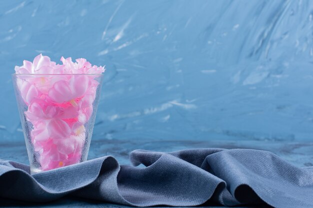 Glass cup with pink petals of flower on blue.