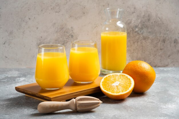 Glass cups of orange juice and a wooden reamer .
