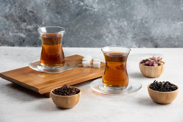 Glass cups of tea with sugar on wooden board.