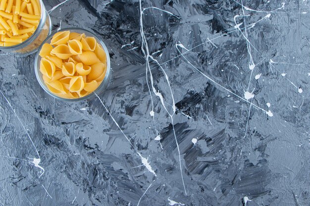 Glass cups of uncooked pasta on a marble background. 