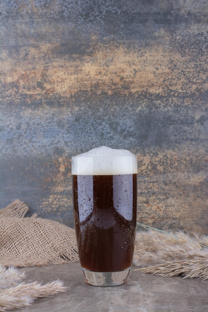 Bicchiere di birra scura con spighe di grano sul tavolo di marmo. foto di alta qualità