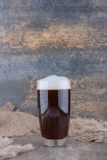 大理石のテーブルに小麦の穂が付いた濃いビールのグラス。高品質の写真