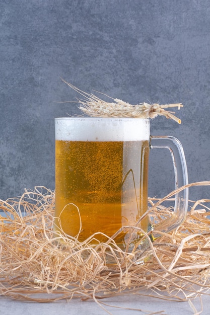 Foto gratuita un bicchiere di birra deliziosa con grano sulla superficie del fieno
