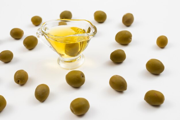 Glass filled with oil surrounded by green olives