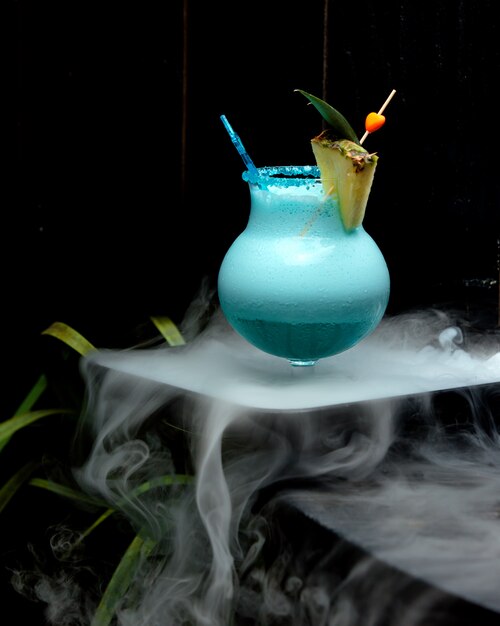 glass of foamy blue cocktail garnished with pineapple slice