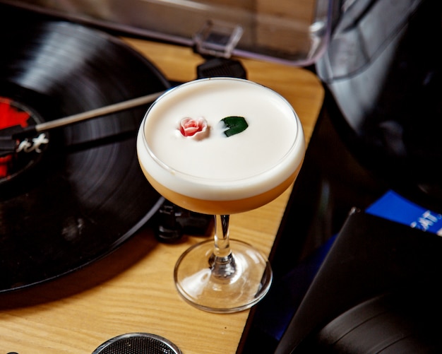 A glass of foamy cocktail decorated with flower and leaf