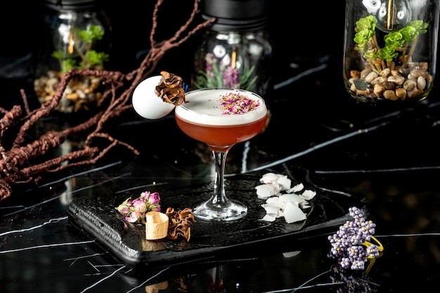 glass of foamy cocktail garnished with dried rose petal pieces and egg shell