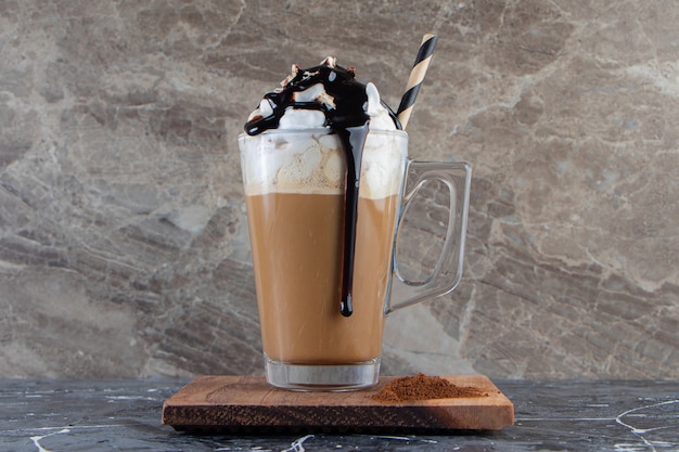 Glass of foamy cold coffee with whipped cream and chocolate on wooden plate. 