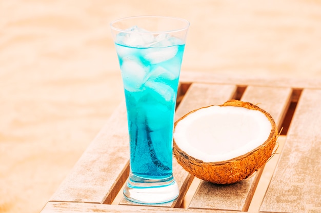 Foto gratuita bicchiere di bevanda blu fresca e cocco spezzato al tavolo di legno