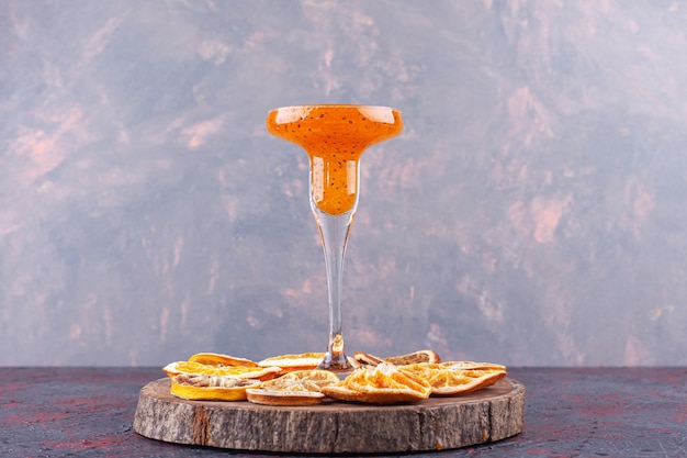 Glass of fresh cocktail and dried citrus fruits on wood piece.