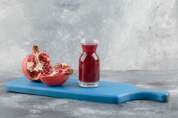 Glass of fresh juice with ripe pomegranate fruits on blue board.