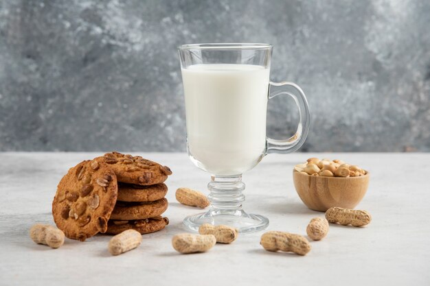 Glass of fresh milk and tasty biscuits with peanuts on marble table. 