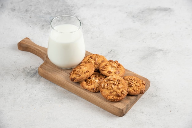 Glass of fresh milk and tasty biscuits on wooden cutting board. 