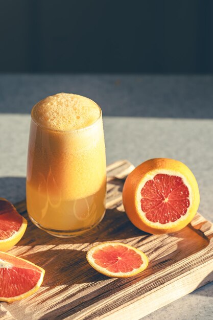 A glass of freshly squeezed juice and orange fruit on a wooden cutting board