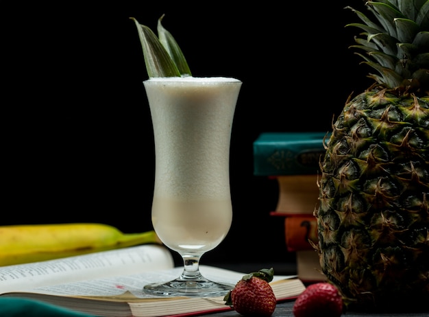 Free photo a glass of full mixed tropical fruits cocktail standing on a book leaves