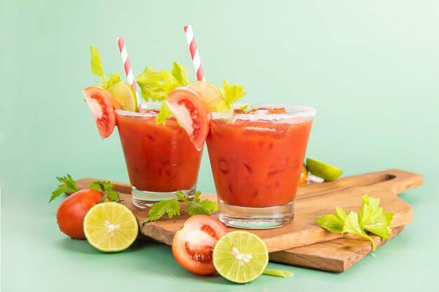 Glass glass of tomato juice, lime with fresh bright bunch of tomatoes isolated on green background, green parsley. vegetable drink.