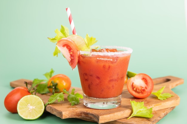 Glass glass of tomato juice, lime with fresh bright bunch of tomatoes isolated on green background, green parsley. vegetable drink.