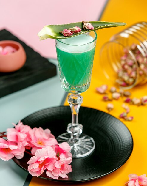 glass of green cocktail garnished with aloe leave and dried rose buds