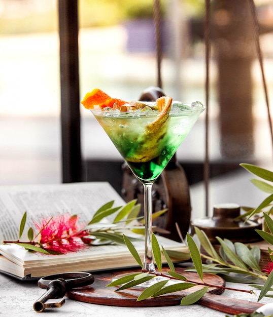 glass of green cocktail garnished with orange zest banana peel and kiwifruit