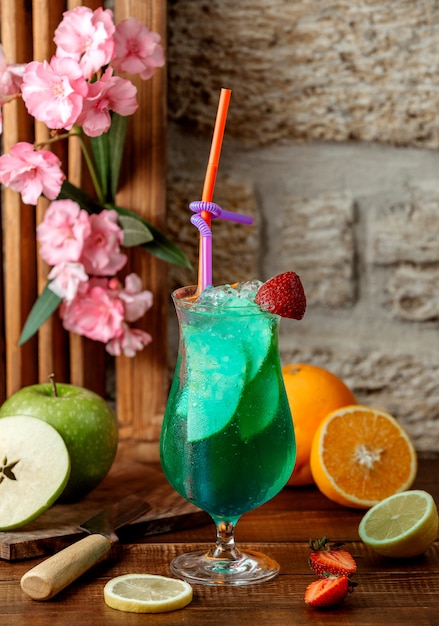 Glass of green cocktail with apple slices, ice and strawberry