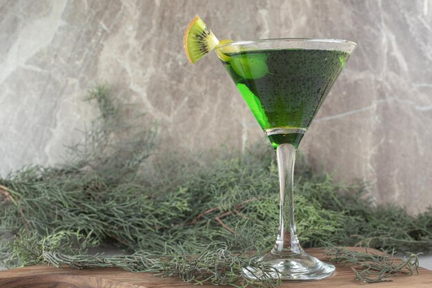 A glass of green cocktail with kiwi slices on wooden board